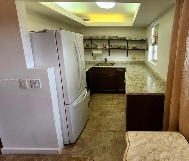 kitchen with white refrigerator, light stone countertops, dark brown cabinetry, and sink