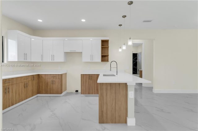 kitchen featuring kitchen peninsula, white cabinetry, sink, and hanging light fixtures