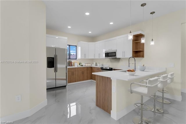 kitchen featuring kitchen peninsula, appliances with stainless steel finishes, a breakfast bar, pendant lighting, and white cabinets