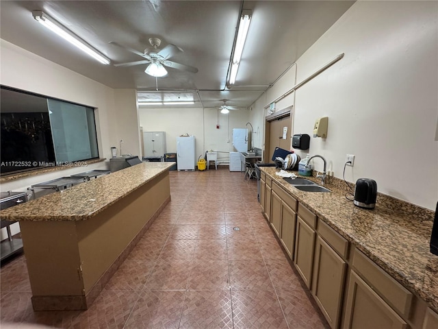 kitchen featuring a center island, white fridge, sink, stone countertops, and ceiling fan