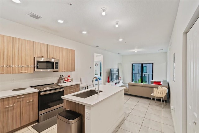 kitchen with an island with sink, stainless steel appliances, sink, and light tile patterned floors