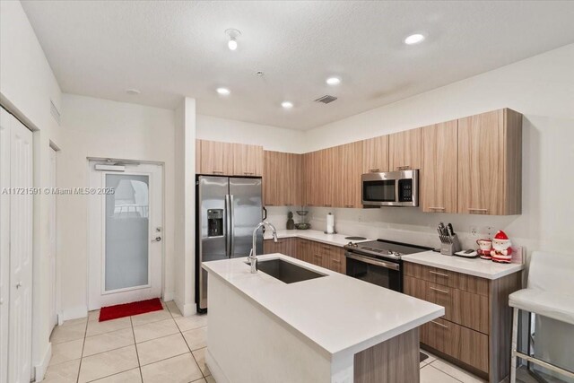 kitchen with light tile patterned flooring, sink, a center island with sink, a textured ceiling, and appliances with stainless steel finishes