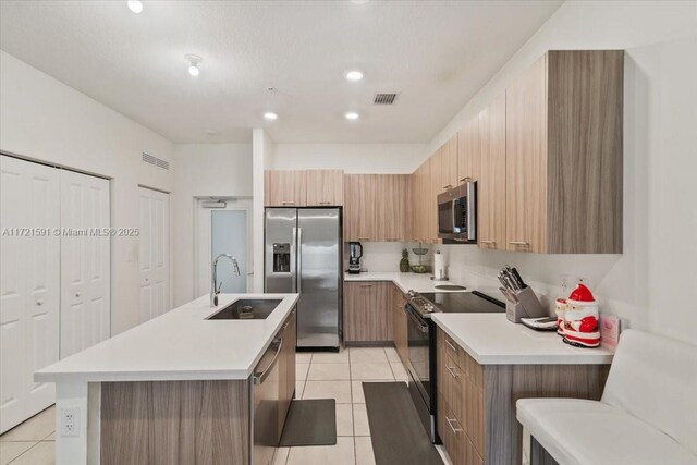 kitchen with sink, light tile patterned floors, a kitchen breakfast bar, stainless steel appliances, and a center island