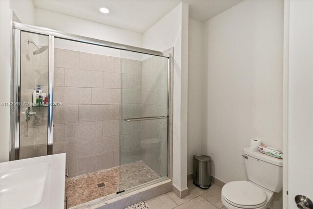 bathroom featuring tile patterned flooring, sink, a shower with shower door, and toilet