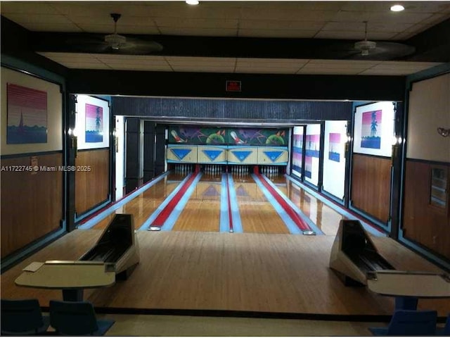 game room with a paneled ceiling, ceiling fan, bowling, and wooden walls