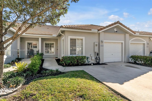 view of front facade featuring concrete driveway, an attached garage, a tiled roof, and stucco siding