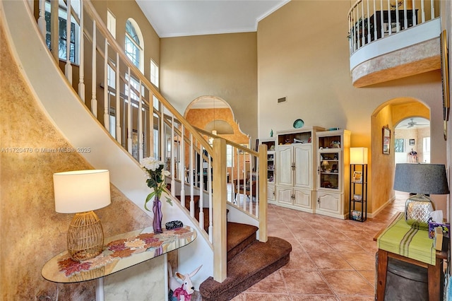 stairs featuring ceiling fan, tile patterned flooring, a towering ceiling, and ornamental molding