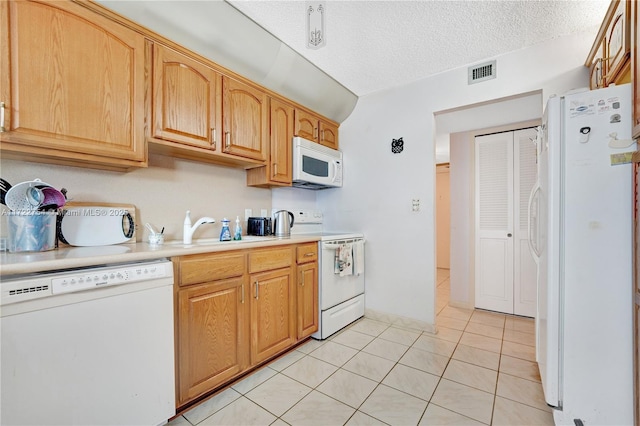 kitchen featuring a textured ceiling, sink, light tile patterned floors, and white appliances