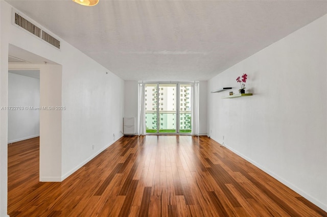 empty room featuring baseboards, floor to ceiling windows, visible vents, and wood finished floors