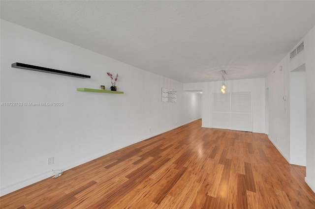 empty room with light wood-style flooring, visible vents, and a textured ceiling