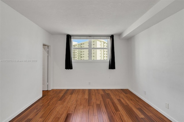 empty room featuring a textured ceiling, dark wood-type flooring, and baseboards