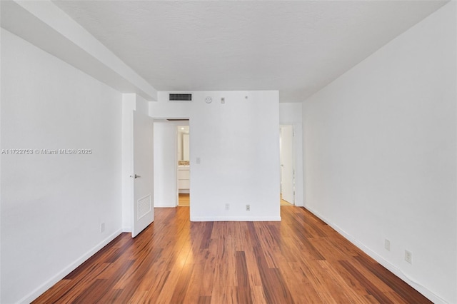 empty room with dark wood finished floors, visible vents, and baseboards