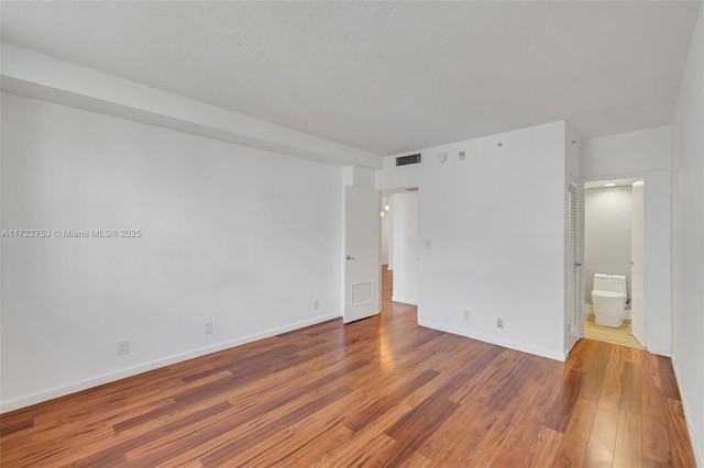 spare room featuring wood finished floors, visible vents, and baseboards