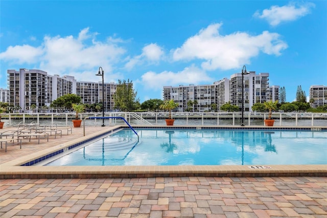 community pool with a patio area, fence, and a city view