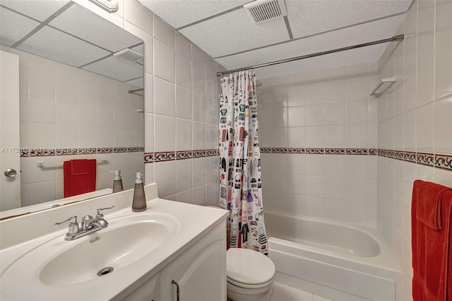 full bathroom with a paneled ceiling, vanity, toilet, shower / bath combo with shower curtain, and tile walls