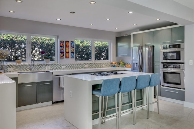 kitchen with a center island, a breakfast bar area, backsplash, gray cabinets, and appliances with stainless steel finishes