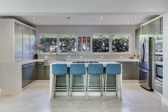 kitchen featuring tasteful backsplash, a kitchen bar, gray cabinets, appliances with stainless steel finishes, and sink