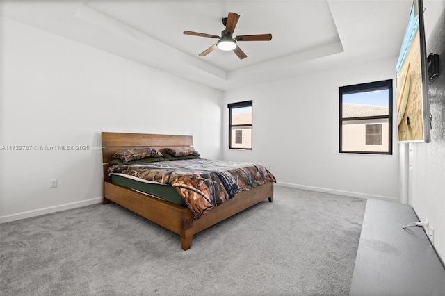 carpeted bedroom featuring a raised ceiling, multiple windows, and ceiling fan