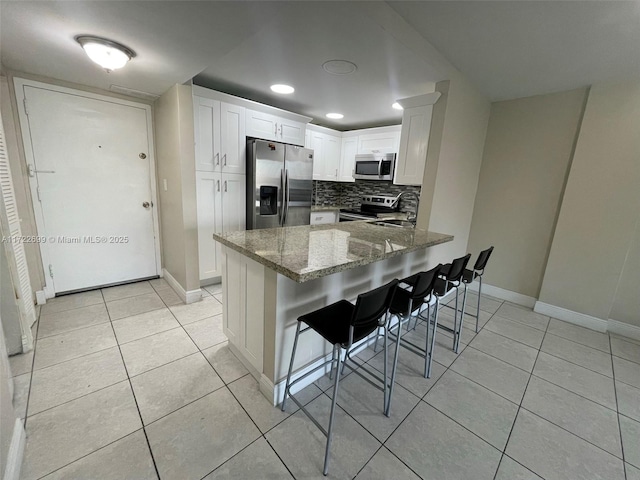 kitchen featuring white cabinets, a kitchen breakfast bar, stone countertops, kitchen peninsula, and stainless steel appliances