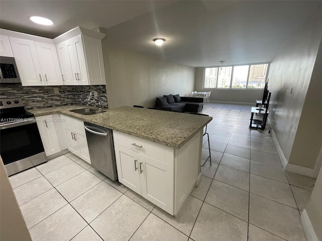 kitchen with light stone countertops, white cabinetry, sink, stainless steel appliances, and kitchen peninsula