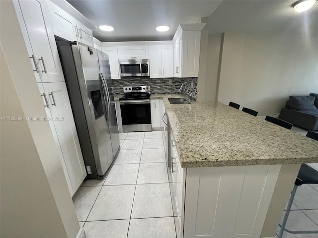 kitchen with white cabinets, sink, decorative backsplash, a kitchen bar, and stainless steel appliances