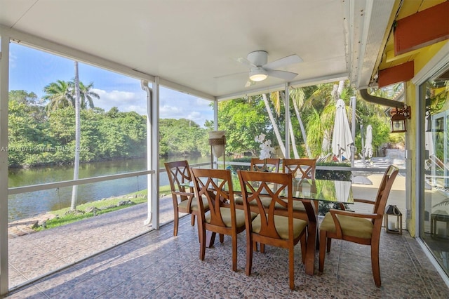 sunroom with ceiling fan and a water view