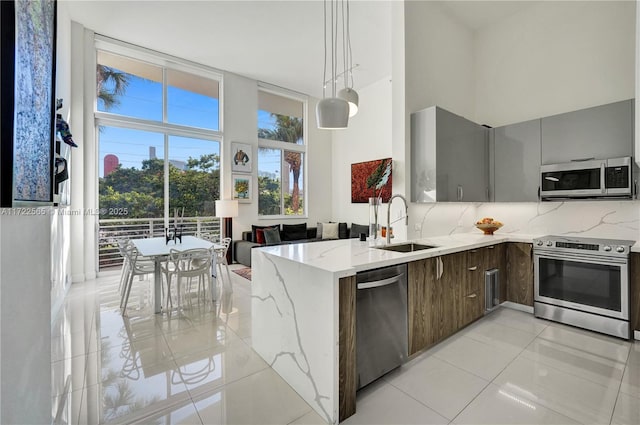 kitchen featuring sink, light tile patterned floors, light stone counters, kitchen peninsula, and stainless steel appliances