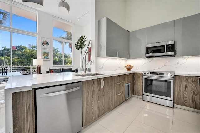 kitchen featuring sink, tasteful backsplash, kitchen peninsula, light tile patterned floors, and appliances with stainless steel finishes