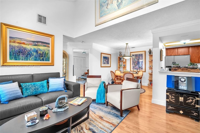 living room featuring a textured ceiling, ornamental molding, light hardwood / wood-style floors, and ceiling fan