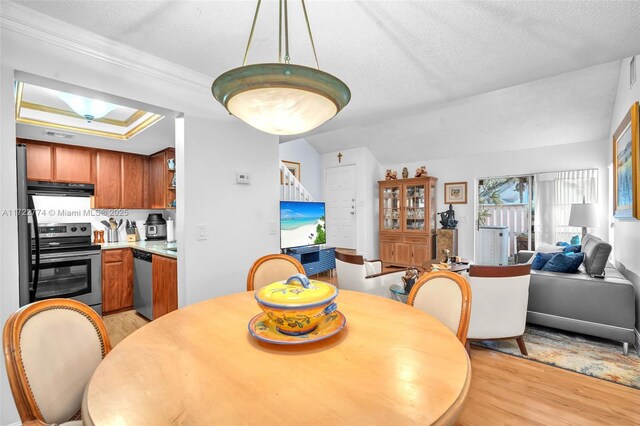 dining space with vaulted ceiling, ornamental molding, a textured ceiling, and light wood-type flooring