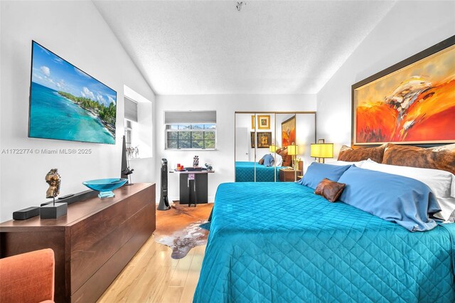 bedroom featuring lofted ceiling, a closet, a textured ceiling, and light wood-type flooring