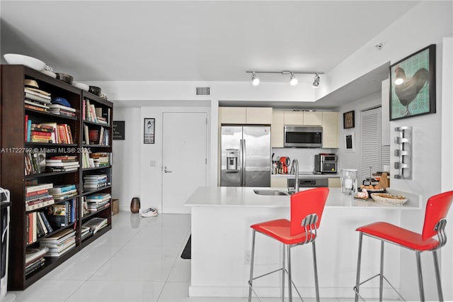 kitchen with appliances with stainless steel finishes, a breakfast bar, sink, light tile patterned floors, and cream cabinets