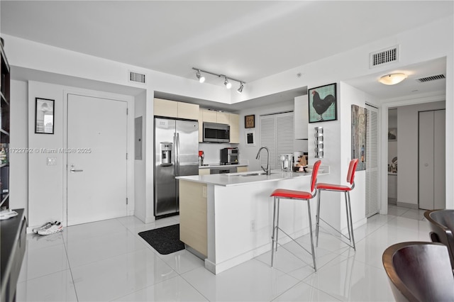 kitchen featuring sink, light tile patterned flooring, a kitchen bar, kitchen peninsula, and stainless steel appliances