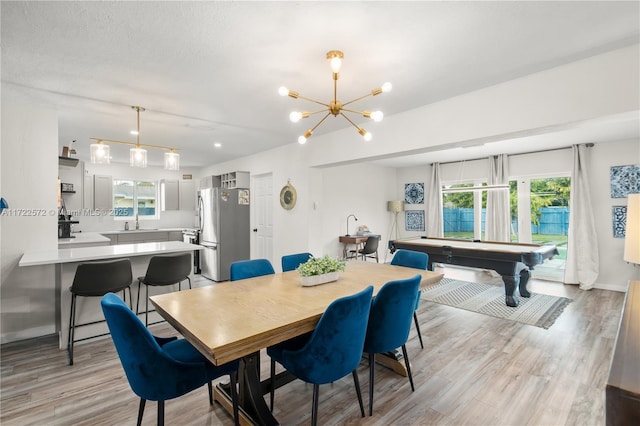 dining space with sink, light hardwood / wood-style flooring, a textured ceiling, pool table, and a notable chandelier