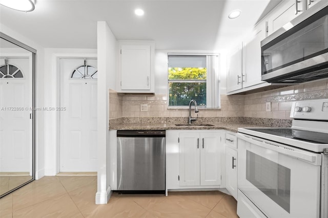 kitchen with stainless steel appliances, sink, light tile patterned floors, dark stone countertops, and white cabinets