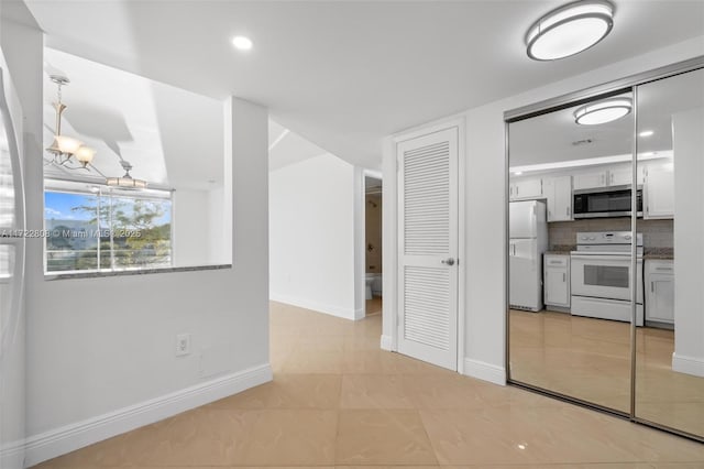 interior space featuring decorative backsplash, white appliances, pendant lighting, a notable chandelier, and white cabinets