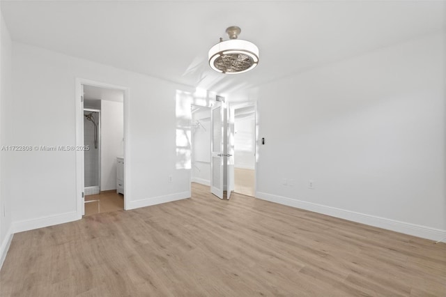 unfurnished bedroom featuring light wood-type flooring, connected bathroom, and a spacious closet