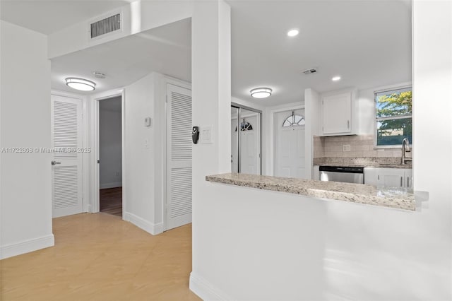 kitchen with light stone countertops, sink, stainless steel dishwasher, backsplash, and white cabinets