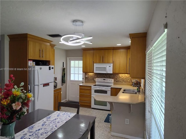 kitchen with backsplash, white appliances, sink, decorative light fixtures, and a chandelier