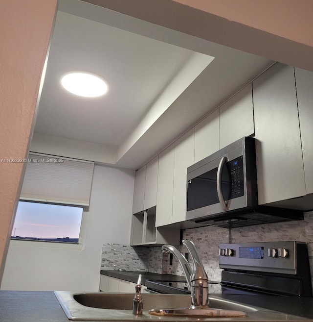 kitchen featuring a raised ceiling, backsplash, white cabinetry, and sink