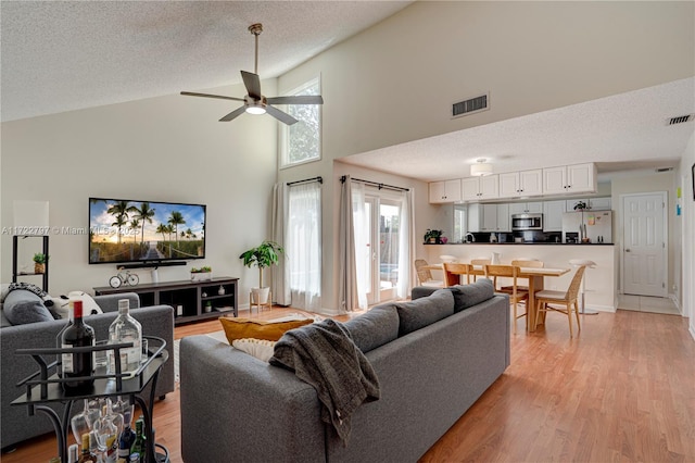 living area with a textured ceiling, ceiling fan, light wood-style flooring, visible vents, and vaulted ceiling