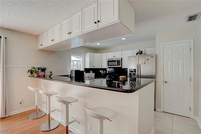 kitchen with white cabinetry, a breakfast bar, appliances with stainless steel finishes, and kitchen peninsula