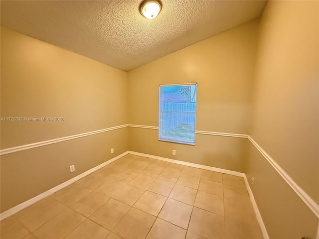 empty room featuring vaulted ceiling, tile patterned flooring, and a textured ceiling