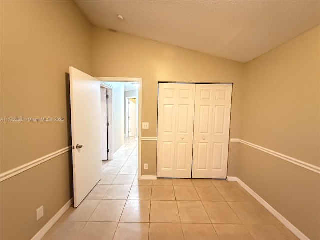 unfurnished bedroom with lofted ceiling, light tile patterned floors, and a closet