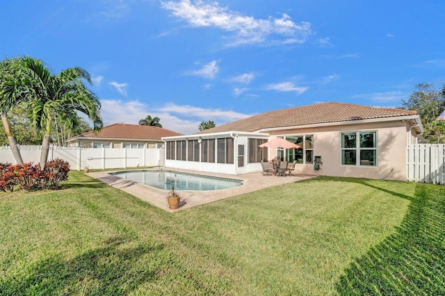 rear view of property with a sunroom, a patio area, a fenced in pool, and a lawn