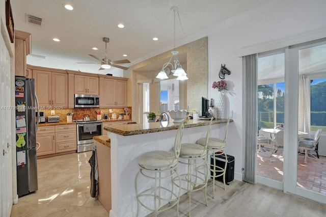 kitchen featuring kitchen peninsula, appliances with stainless steel finishes, light stone counters, ceiling fan with notable chandelier, and decorative light fixtures