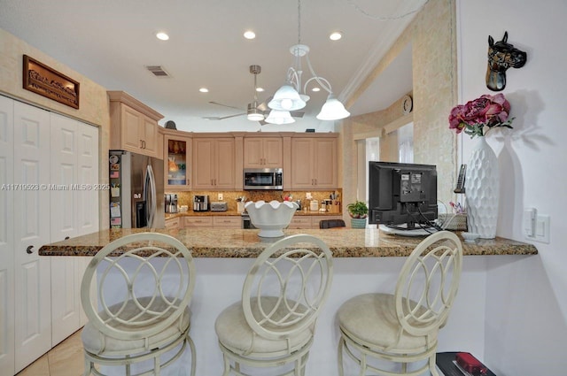 kitchen with kitchen peninsula, appliances with stainless steel finishes, a kitchen bar, and light stone counters