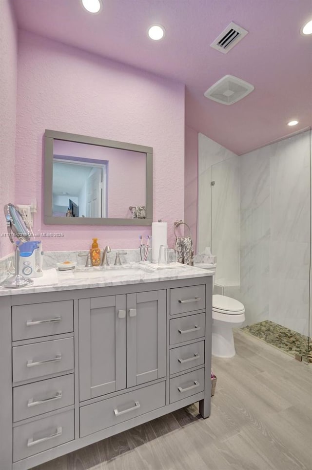 bathroom with a shower, hardwood / wood-style flooring, vanity, and toilet