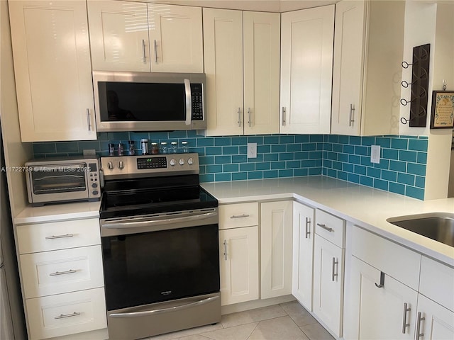 kitchen featuring backsplash, white cabinetry, stainless steel appliances, and light tile patterned floors