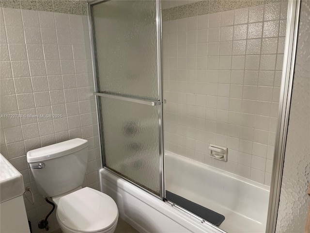 full bathroom featuring vanity, combined bath / shower with glass door, tile walls, and toilet